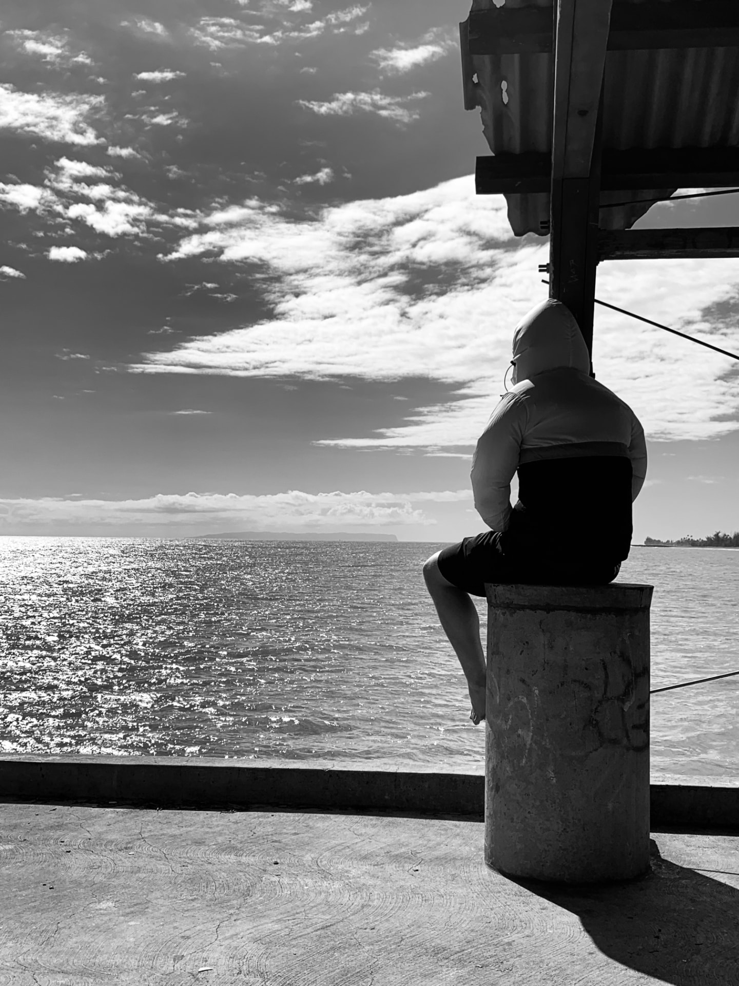 A hooded figure seated at the edge of the sea, looking out over the water